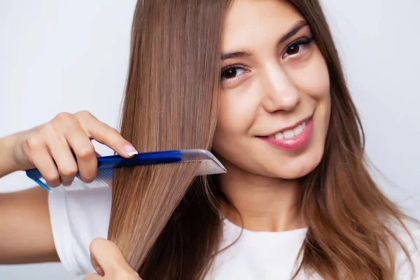 Bella giovane donna si prende cura dei suoi capelli, pettinando i capelli lunghi con un pettine — Foto Stock