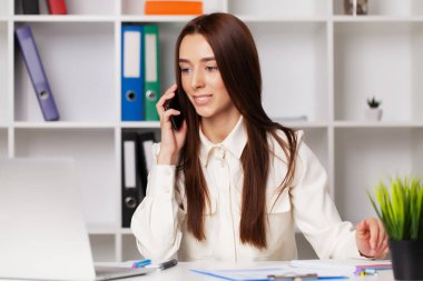 Ofiste dizüstü bilgisayarla çalışırken telefonda konuşan güzel bir bayan yönetici.