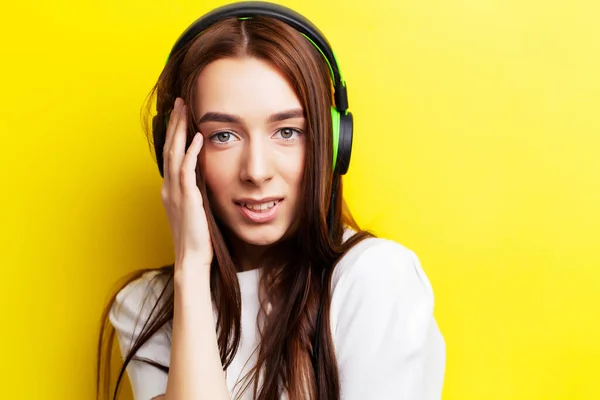 Beautiful young girl model listens to music in headphones on a yellow background — Stock Photo, Image
