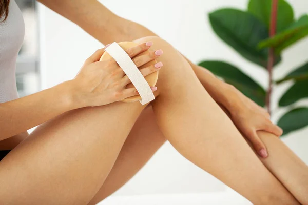 Brazo de mujer sosteniendo cepillo seco en la parte superior de su pierna, tratamiento de celulitis y cepillado en seco . — Foto de Stock