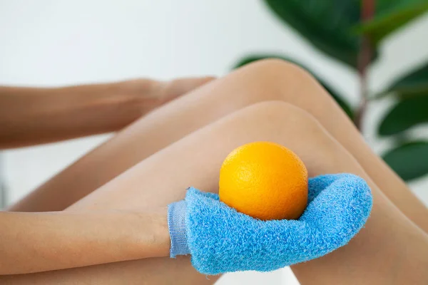 Braço das mulheres segurando escova seca para cima de sua perna e laranja, tratamento de celulite e escovação seca . — Fotografia de Stock