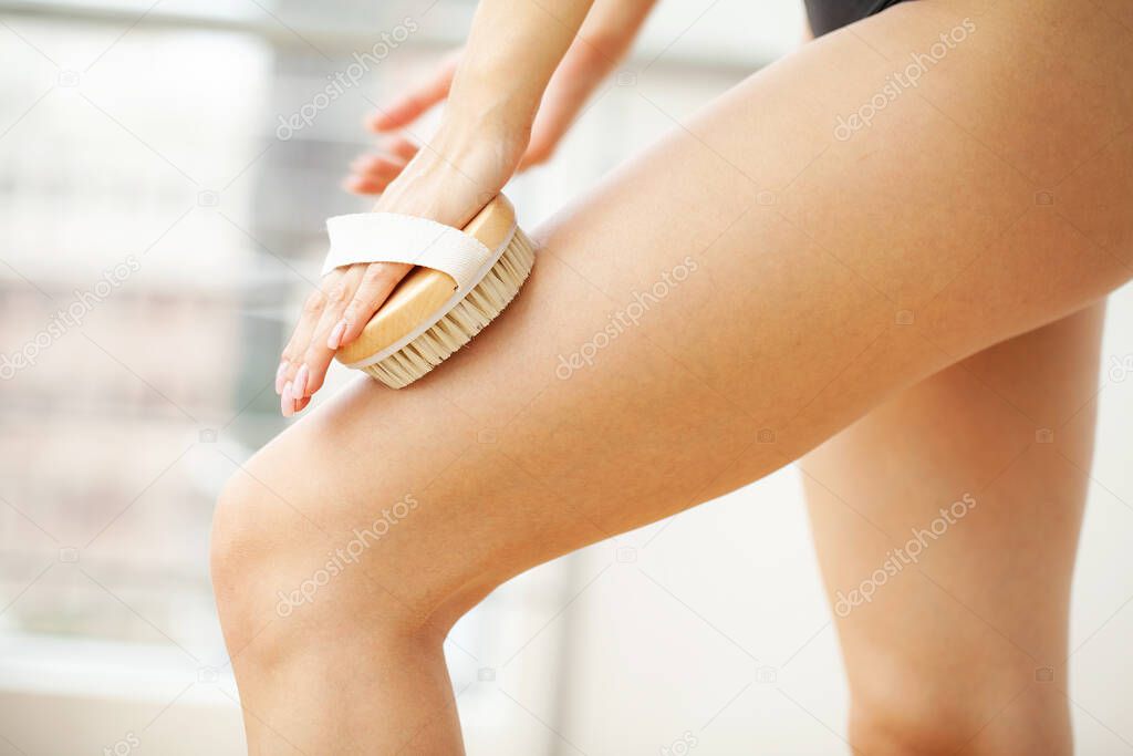 Womans arm holding dry brush to top of her leg, cellulite treatment and dry brushing.
