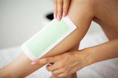 Ayaklarında güzel deri olan bir kadın, tüylerini aldırmak için bacağına balmumu bandı yapıştırıyor.