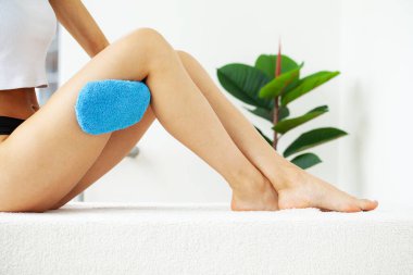 Bacağının üst kısmında mavi kuru fırça tutan kadın kolu, selülit tedavisi ve kuru fırça..