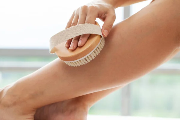 Tratamento de celulite, braço de mulher segurando escova seca para cima de sua perna. — Fotografia de Stock