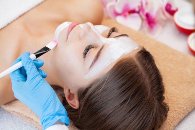 Güzellik salonunda usta ve müşteri, yüz bakımı için beyaz kilden yapılmış bir maske.