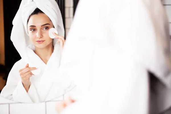 Mujer joven sonriente lavándose la cara con esponja de limpieza facial en el baño — Foto de Stock