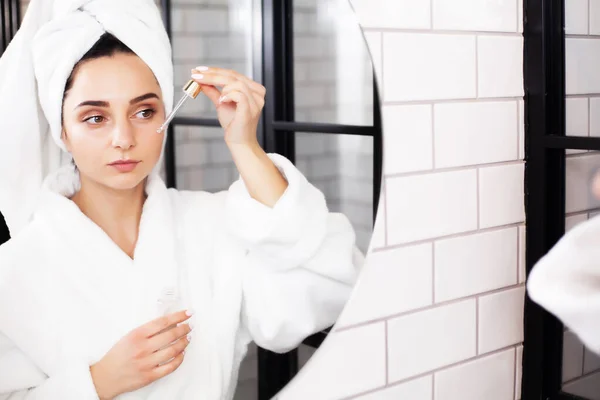 Mujer joven después de la ducha va a aplicar productos para el cuidado de la piel, aceite o suero. — Foto de Stock