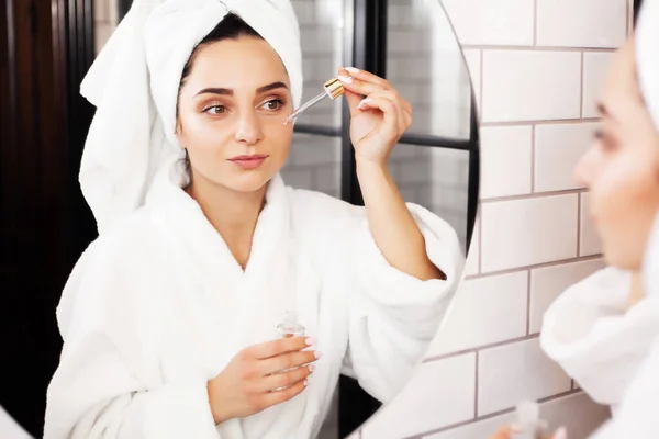 Mujer joven después de la ducha va a aplicar productos para el cuidado de la piel, aceite o suero. — Foto de Stock