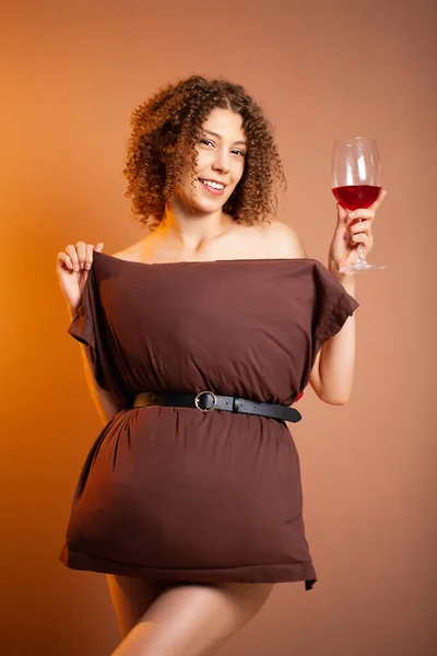 Beautiful woman with a glass of red wine and a pillow instead of a dress — Stock Photo, Image