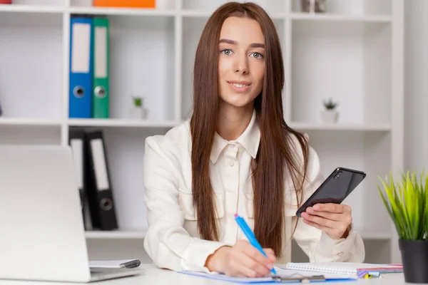 Atrakcyjna kobieta pracująca na smartfonie na swoim stanowisku pracy. — Zdjęcie stockowe