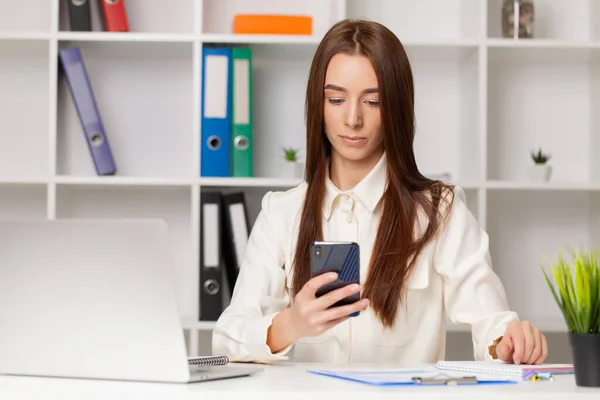 Mujer atractiva trabajando en el teléfono inteligente en su estación de trabajo. — Foto de Stock