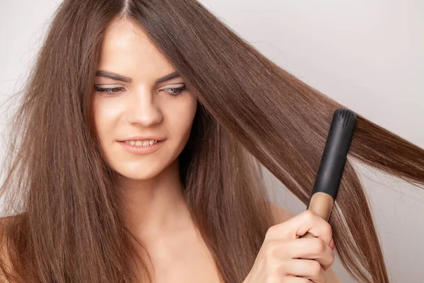 Mujer con hermoso cabello largo y liso usando un alisador de cabello — Foto de Stock