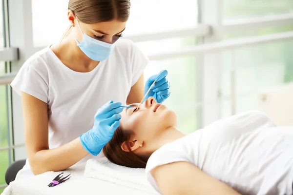 Mooie vrouw met lange wimpers krijgen een wimper uitbreiding procedure in een schoonheidssalon. — Stockfoto