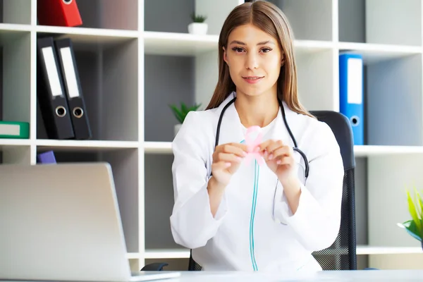 Médico sonriente con cinta rosa para la conciencia del cáncer en el gabinete del hospital — Foto de Stock