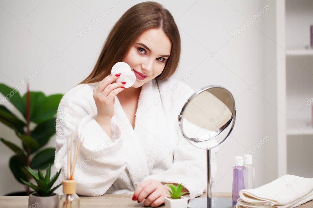 Smiling young woman washing her face with facial cleansing sponge at bathroom