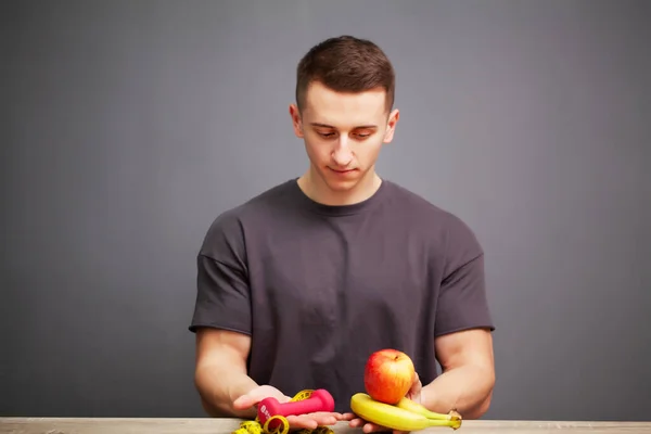 Shaped and healthy body man holding a fresh fruits and junk food