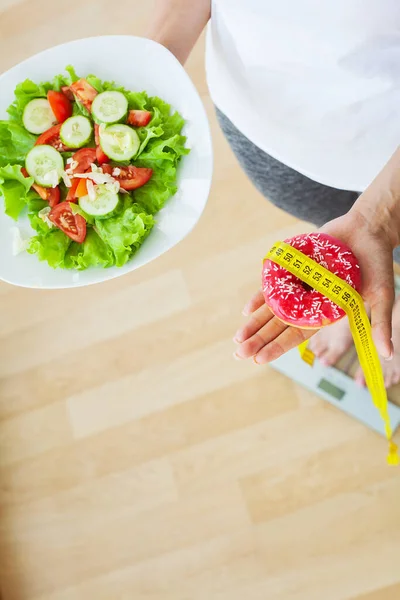 Conceptul de dietă, femeia măsoară greutatea pe cântare electronică în timp ce deține gogoși calorice — Fotografie, imagine de stoc