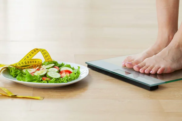 Conceito de dieta, mulher mede peso em balanças eletrônicas e salada de dieta com fita métrica amarela — Fotografia de Stock