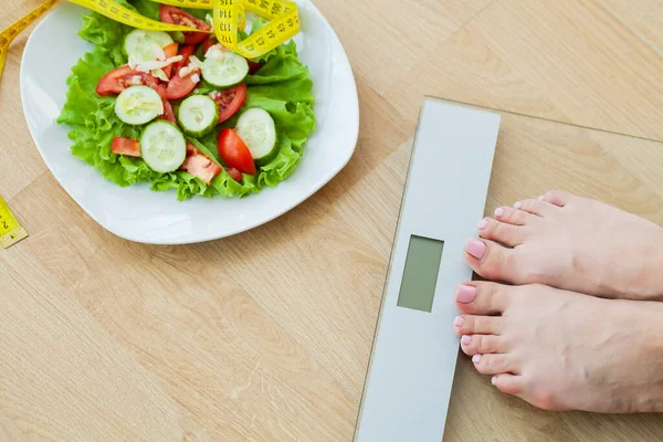 Dieta concetto, donna misura il peso su bilance elettroniche e dieta insalata con nastro di misurazione giallo — Foto Stock