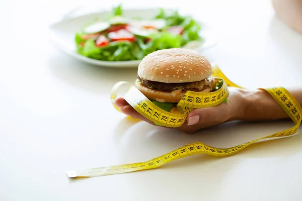 Вредная еда, жирный бургер рядом с желтой измерительной лентой — стоковое фото