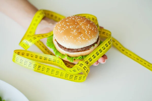 Вредная еда, жирный бургер рядом с желтой измерительной лентой — стоковое фото