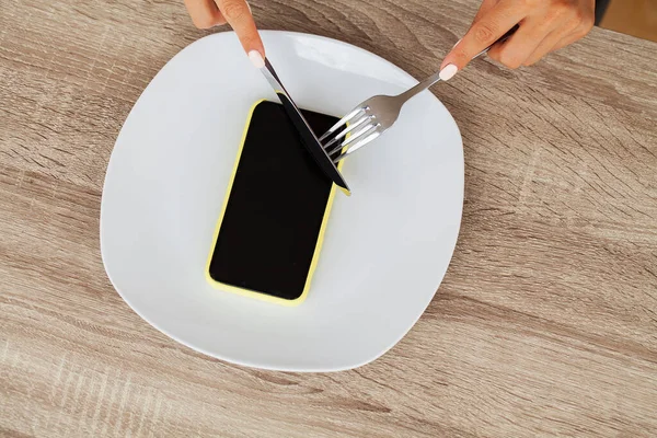 Beroende av telefonen, stäng en kvinna händer håller en gaffel och en kniv över telefonen på plattan — Stockfoto