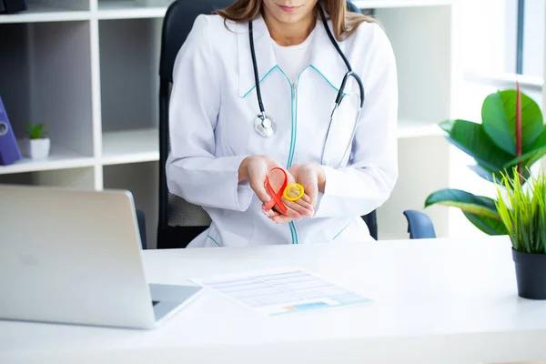 Médico mujer sosteniendo condón y cinta roja para la conciencia de la enfermedad por el VIH — Foto de Stock