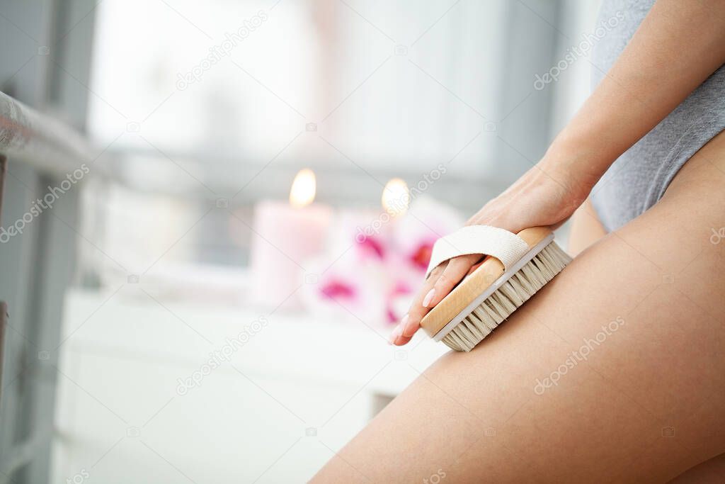 Cellulite treatment, woman arm holding dry brush to top of her leg.