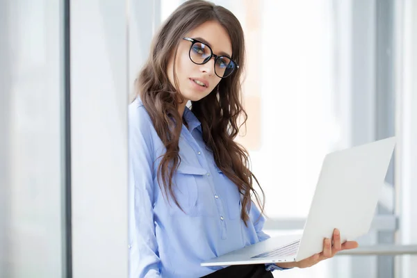 Charmig affärskvinna nära fönstret arbetar på laptop på kontoret — Stockfoto