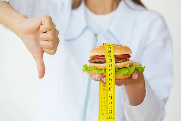 Diet koncept, läkare som håller skadlig fett burgare med gul måttband — Stockfoto