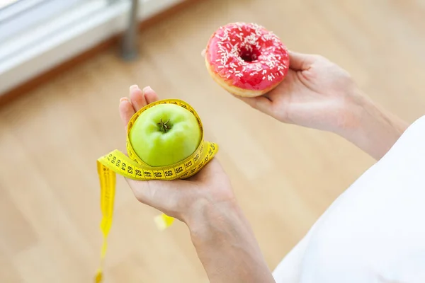 Dieetconcept, vrouw met een keuze uit schadelijke donut en verse appel — Stockfoto