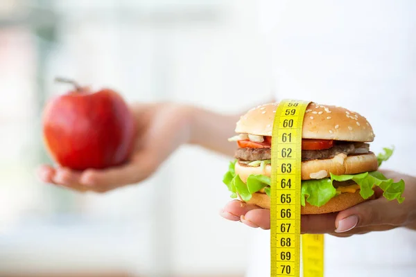 Diet koncept, kvinna som håller ett val av skadlig hamburgare och färska äpple — Stockfoto