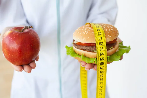 Diet koncept, kvinna som håller ett val av skadlig hamburgare och färska äpple — Stockfoto