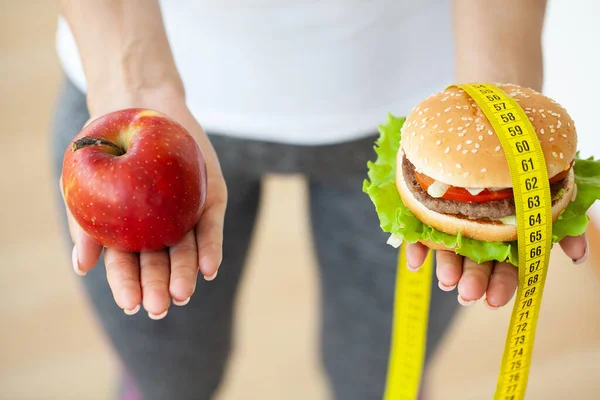 Concepto de la dieta, mujer que sostiene una opción de hamburguesa dañina y manzana fresca —  Fotos de Stock