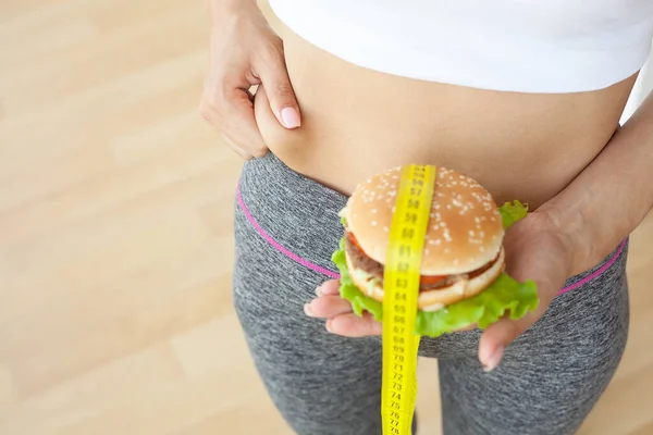饮食概念，妇女持有有害脂肪汉堡与黄色测量带 — 图库照片