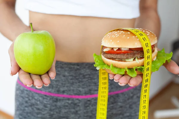 Diet koncept, kvinna som håller ett val av skadlig hamburgare och färska äpple — Stockfoto
