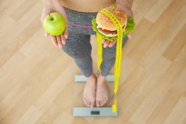 Concepto de la dieta, mujer que sostiene una opción de hamburguesa dañina y manzana fresca — Foto de Stock