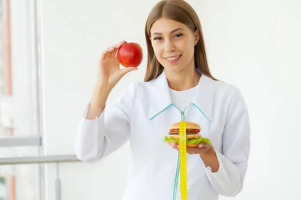 Conceito de dieta, mulher segurando uma escolha de hambúrguer prejudicial e maçã fresca — Fotografia de Stock