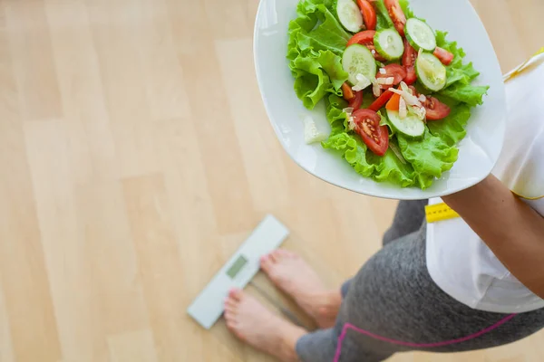 Диетическая концепция, женщина держит свежий салат диеты измерить ее вес — стоковое фото