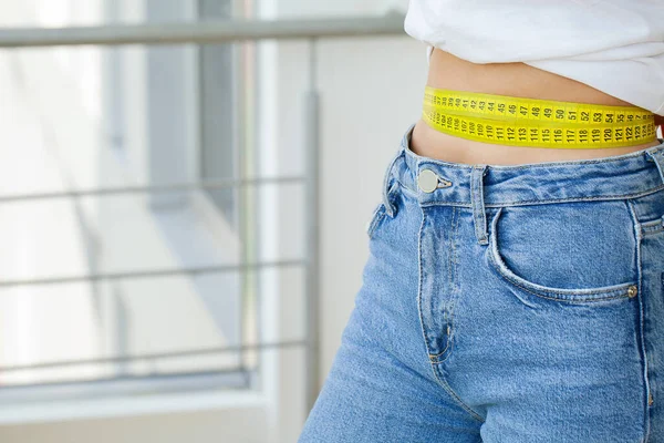 Schlanke Frau in Jeans und weißem T-Shirt misst ihre Taille — Stockfoto