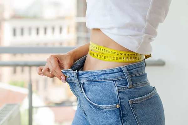 Schlanke Frau in Jeans und weißem T-Shirt misst ihre Taille — Stockfoto