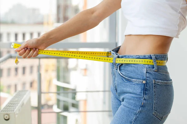 Mujer delgada en jeans y una camiseta blanca mide su cintura — Foto de Stock