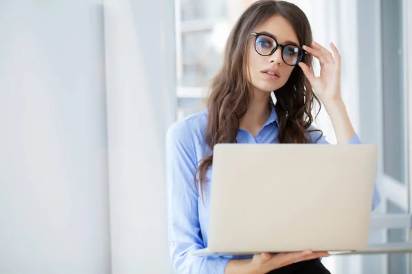 Empresária encantadora perto da janela trabalhando no laptop no escritório — Fotografia de Stock