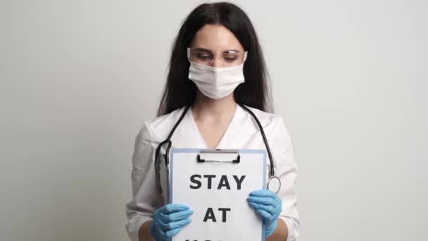 Le médecin dans un masque et gants tient une forme avec l'inscription rester à la maison — Video