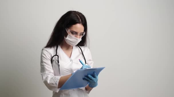 Läkaren i mask och handskar fyller i patientens honungskort — Stockvideo