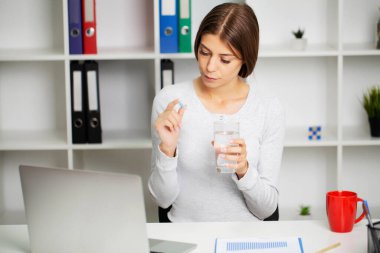 Genç kadın elinde bir bardak suyla beyaz yuvarlak hap alıyor.