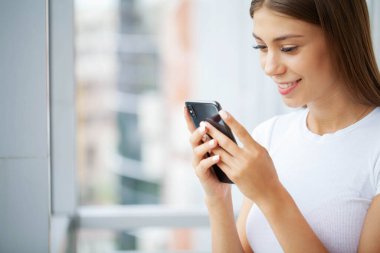 Akıllı telefon tutan, mesaj yazan, sosyal ağlarda arkadaşlarıyla sohbet eden bir kadın.