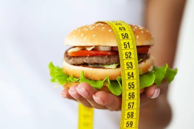 Diyet konsepti: Zararlı yağlı burger ve sarı mezura tutan kadın..