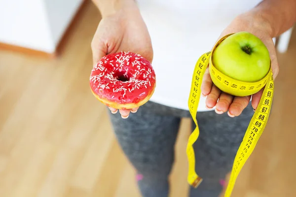 Diet concept, woman holding a choice of harmful donut and fresh apple. — Stock Photo, Image